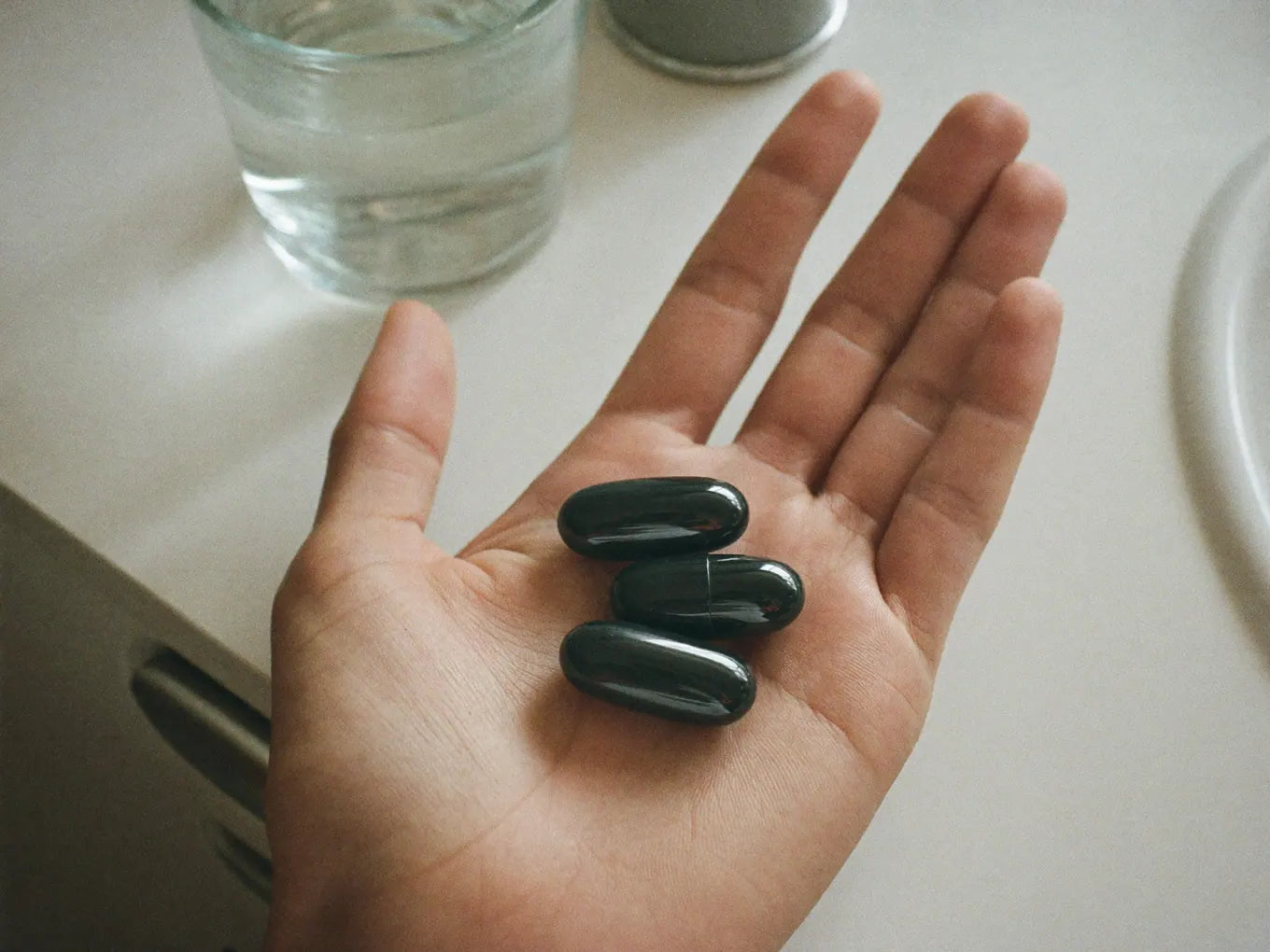 Hand holding three capsules over a glass of water