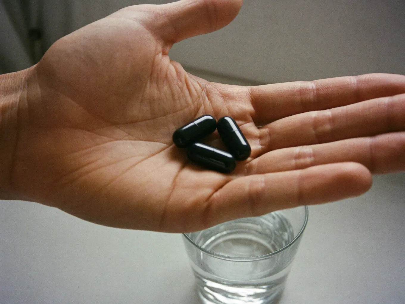Hand holding three capsules over a glass of water