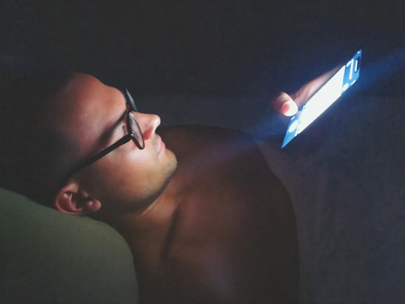 Man lying in bed at night scrolling his phone